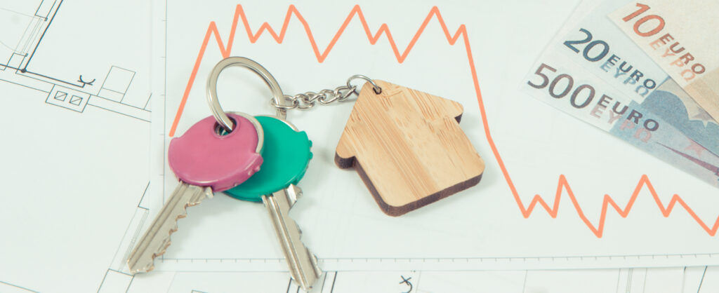 Ein Schlüsselanhänger mit einem Haus und zwei Schlüssel in rosa und grün liegen auf einer abfallenden grafischen Kurve. Daneben ein 500, 20 und 10 Euroschein