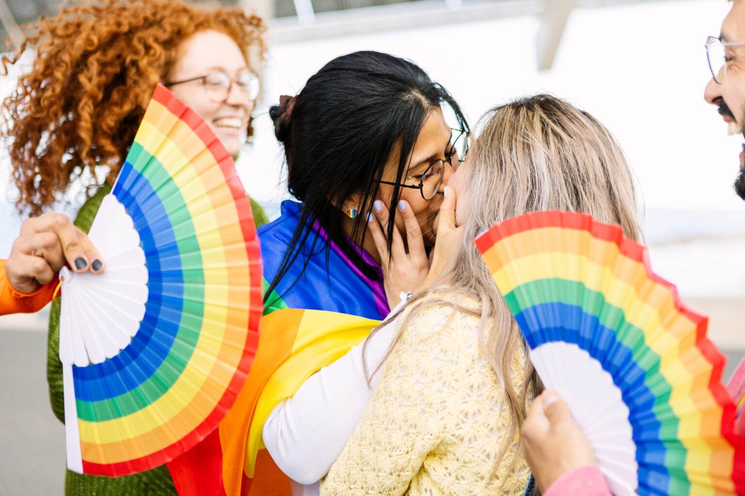 Fächer in bunten Regenbogenfarben die drei Frau halten. Zwei Frauen küssen sich