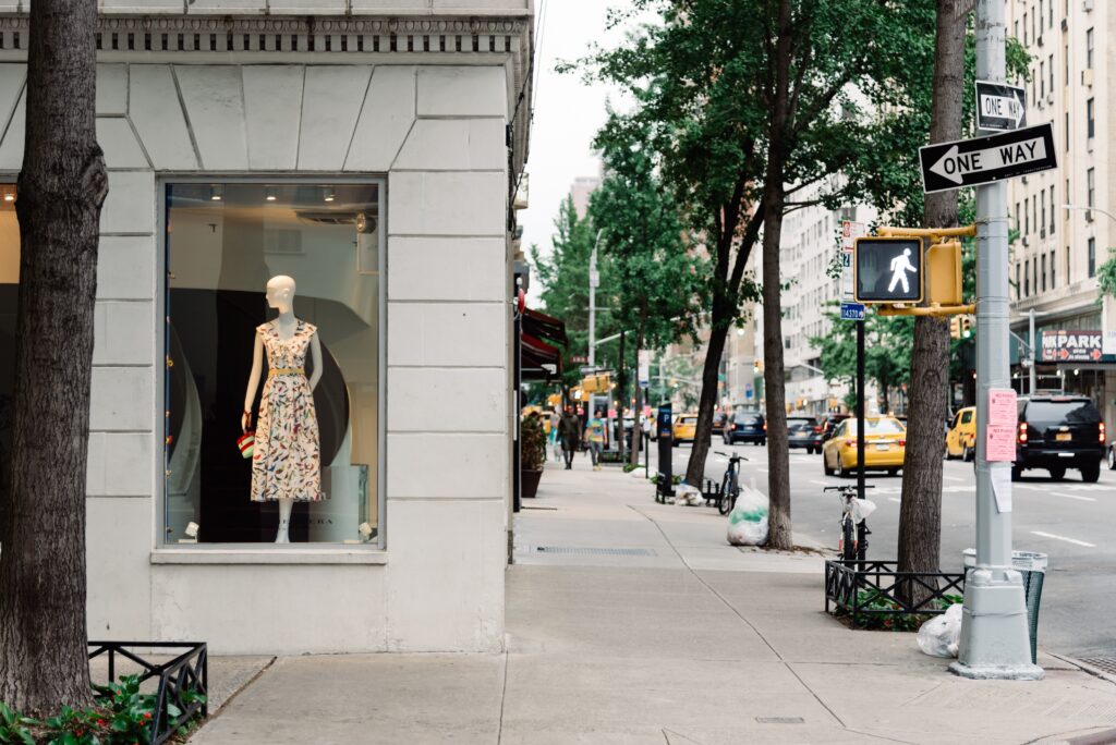 Blick in eine Einkaufsstraße und in ein Kaufhaus, das eine Kleiderpuppe mit einem bunten Sommerkleid präsentiert
